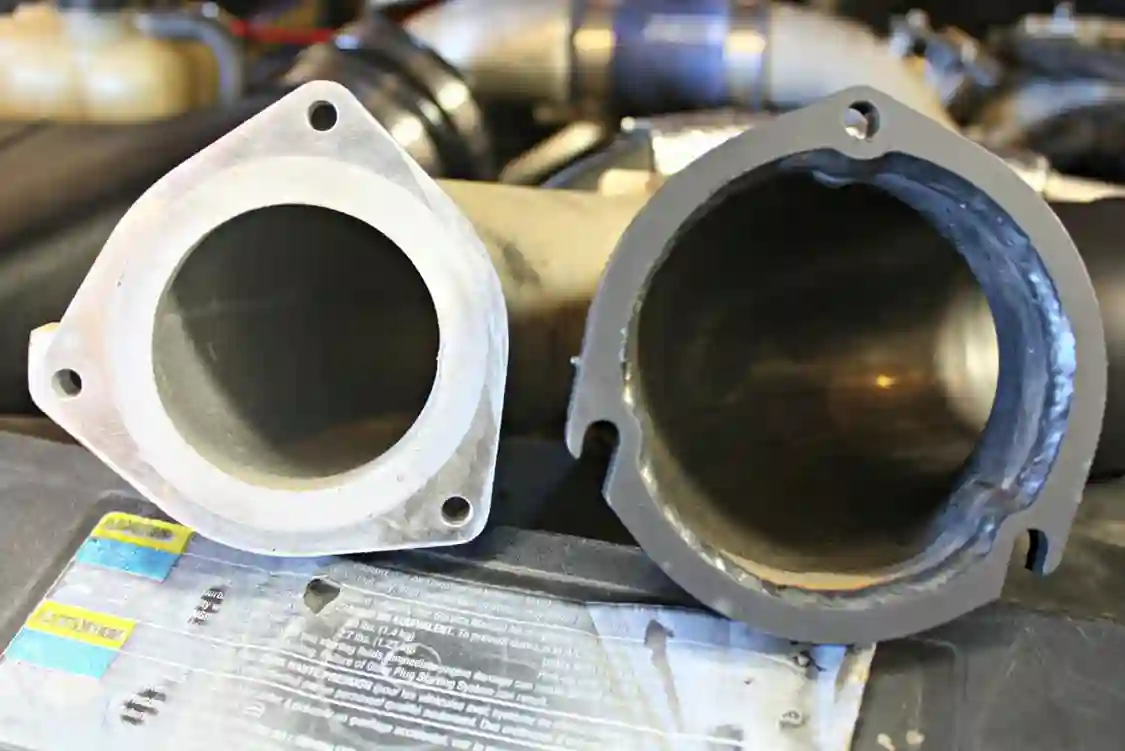 With the factory horn removed you can see the true difference between the factory cast unit and the new DRP fabricated high-flow unit. The large-bore diameter stays consistent from end to end on the DRP piece, while the stock unit bottlenecks down to almost an inch in diameter. You can also see that DRP takes the extra step to aid in installation by slotting the lower mounting bolt holes. This allows you to start those hard to reach bolts into the turbo before slipping the horn into place.