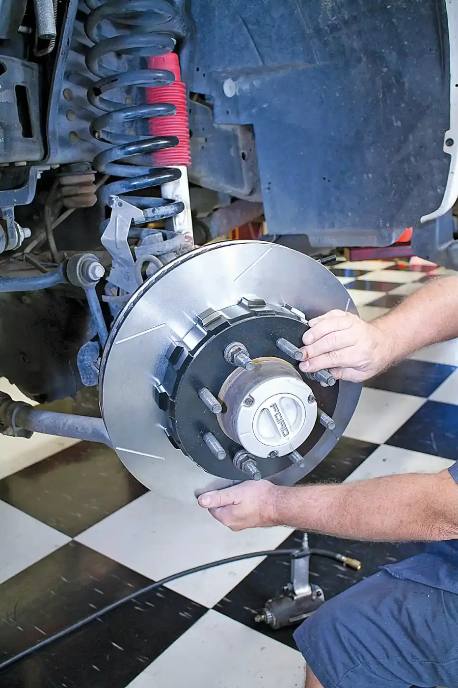 6. The new Wilwood brake rotor and hat are installed over the hub assembly. Using a stock lug nut to hold them down to the hub face makes caliper installation easier. Three lug nuts, finger tight is all you need. This may be done a few times while the caliper center is set on the caliper brackets.