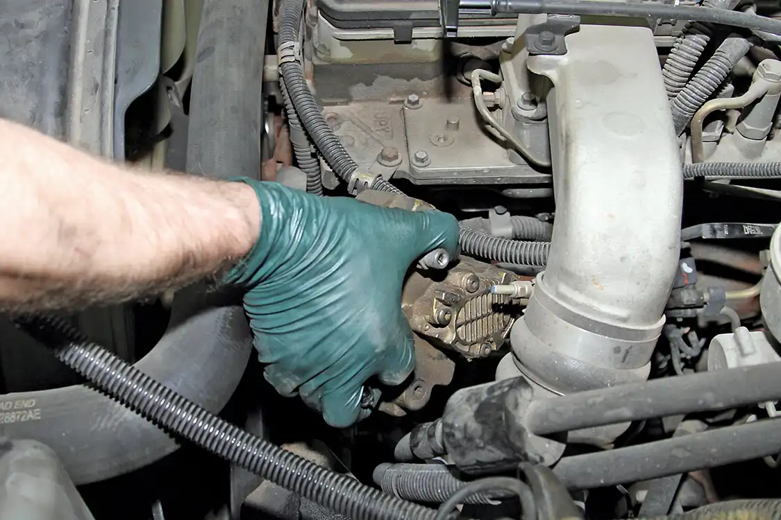 10. Grubb removed the three mounting nuts securing the CP3 and used a prybar to gently loosen the pump from the front cover housing. He then lifted the old CP3 from the front cover housing. He finally lifted the old CP3 out of the engine bay.