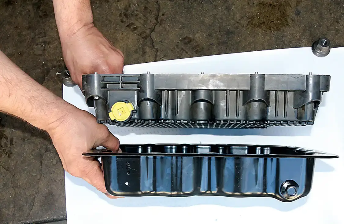 7. This view shows the outside of the composite pan, (top) and the new stamped steel pan bottom. The depth is about the same, but the drain plug position is in opposite corners. 