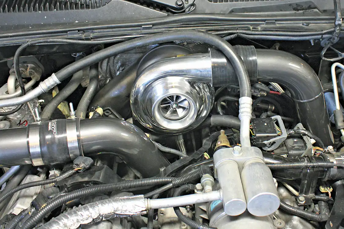 8. The BorgWarner S300 turbocharger fits perfectly under the cowl, resting upon the newly installed pedestal and riser block. The included two-piece downpipe can then be slipped up from below and attached to the turbo's exhaust housing using the supplied v-band clamp. The driver's-side intercooler pipe is also installed using the new boots and clamps.