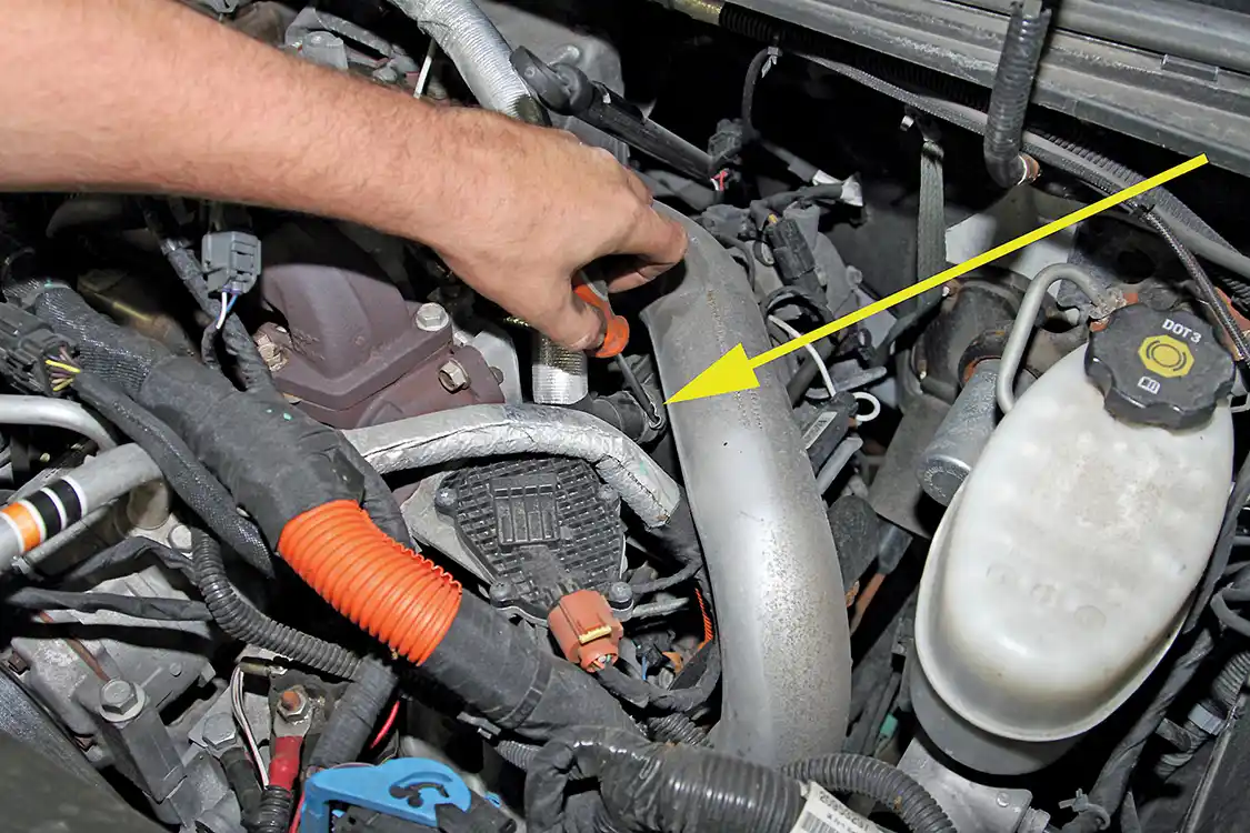 8. To begin rerouting the factory PCV line, start by removing the crimped clamp on the line (see arrow) that connects to the valve cover below the turbo boost tube.