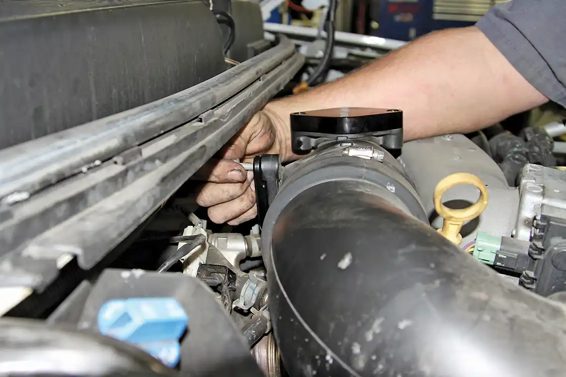 14. Then install the included block off plate to replace the PCV hose assembly and reuse the factory mounting bolts to secure the plate. Be sure to position the wire harness bracket under the lower bolt once again so that it is secure in the engine bay as shown.