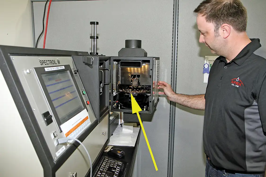 13. After loading the sample tray into the Spectrometer (see arrow) Rainey closes the machine and runs the test for both samples. The Spectrometer is used for elemental testing; it measures elements contained within the oil specifically looking for wear metals, contaminants and oil additives in PPM (Parts Per Million).