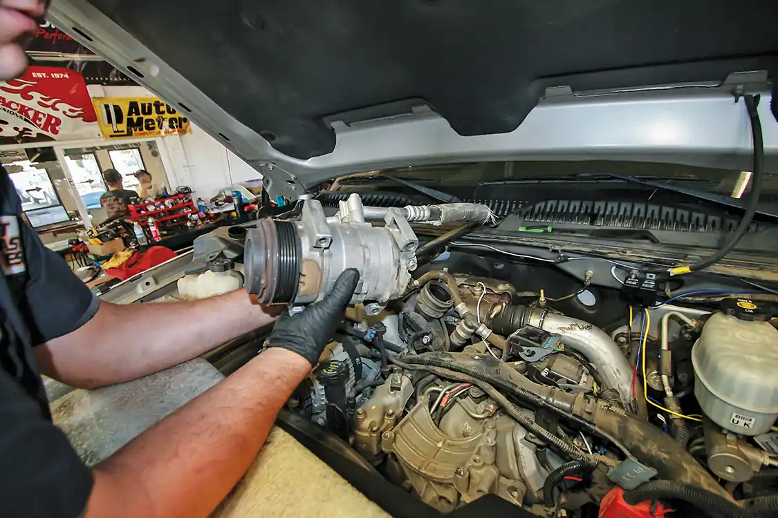 9. There are two sides to the fuel rail on a Duramax, so two of the ported fuel rail fittings are needed. We begin on the passenger’s side by moving the A/C compressor out of the way to gain access underneath.