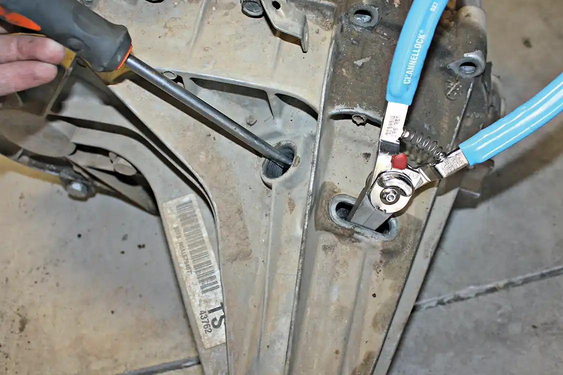 12. With the snap ring pliers holding the snap ring open, a long flathead screwdriver can be slid in through the speed sensor port to help slide the tail shaft forward, releasing the hold within the rear transfer case housing.