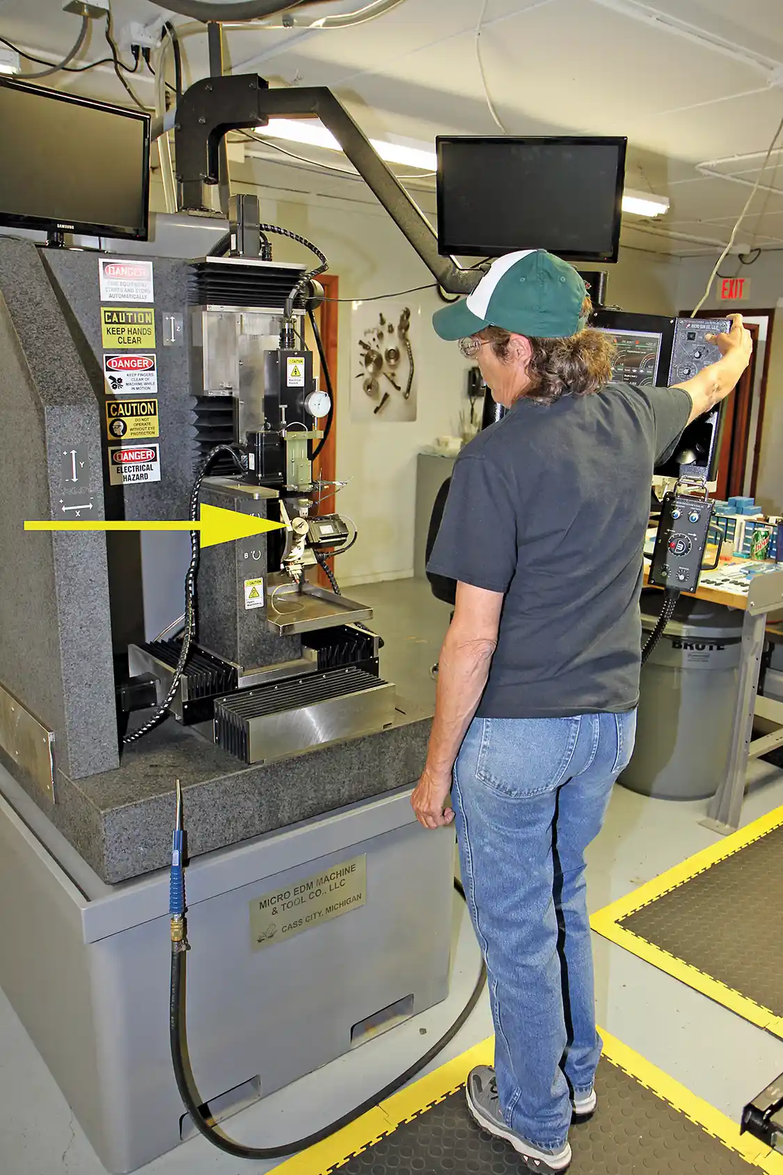 1. Linda Geiger operates the EDM equipment used to enlarge the openings in the injector nozzles in a precise and controlled method. Notice the small injector nozzle at the tip of the arrow compared to the size of the machining equipment.