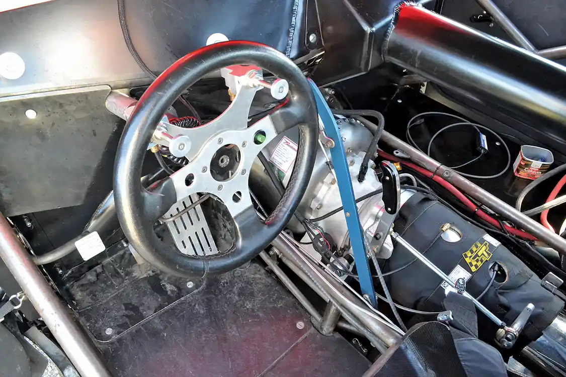 The interior is all business, with a carbon dash, minimal interior and tubular steering column. The black cover for the transmission is a transmission blanket, which protects the driver from any flying parts should breakage occur.