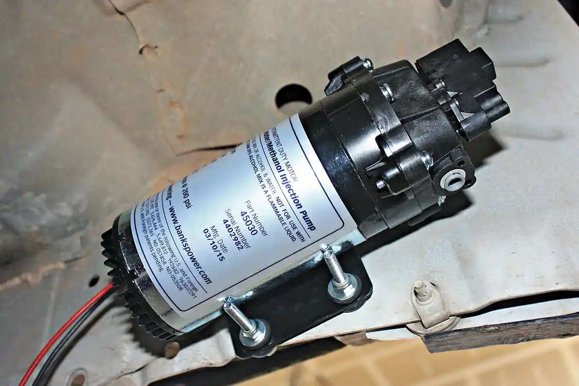 17. Using the water injection pumps bracket as a template, four holes can be drilled on the lower pinch weld area of the cab. The pump will need to be mounted in a safe spot, where road debris and water won’t damage it. The high volume pump supplied in the Double Shot kit features a built-in pressure switch for low fluid and leak detection, a fully adjustable pressure regulator and integral push-lock fittings for easy install.