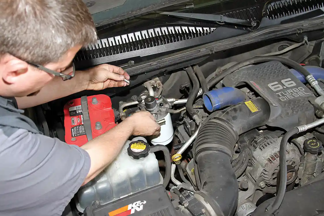 24. Phaff installs the complete assembly on the engine using the longer mounting bolts supplied with the kit. He starts each bolt into the threads in the filter head, leaving room for the spacer to be installed.