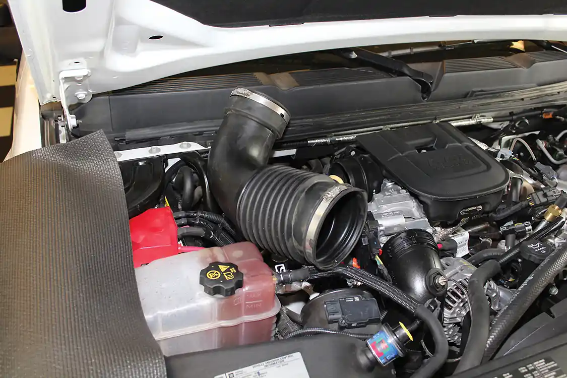3. The first stage of the process is removing the factory intake system. Before you do anything, disconnect the negative cables on both batteries. This helps prevent check engine lights and also forces the engine to re-learn its tuning once the installation is complete. The stock intake tube is held in place with simple worm clamps, while the intake box itself is removed by pulling upward firmly to release the box from its rubber grommets. Use caution when removing the stock intake to make sure you don’t damage any wiring or other under-hood components.